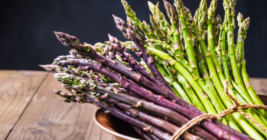 Asparagi verdi e viola in un cestino rustico, ideali per un'alimentazione equilibrata in caso di colite ma con precauzioni